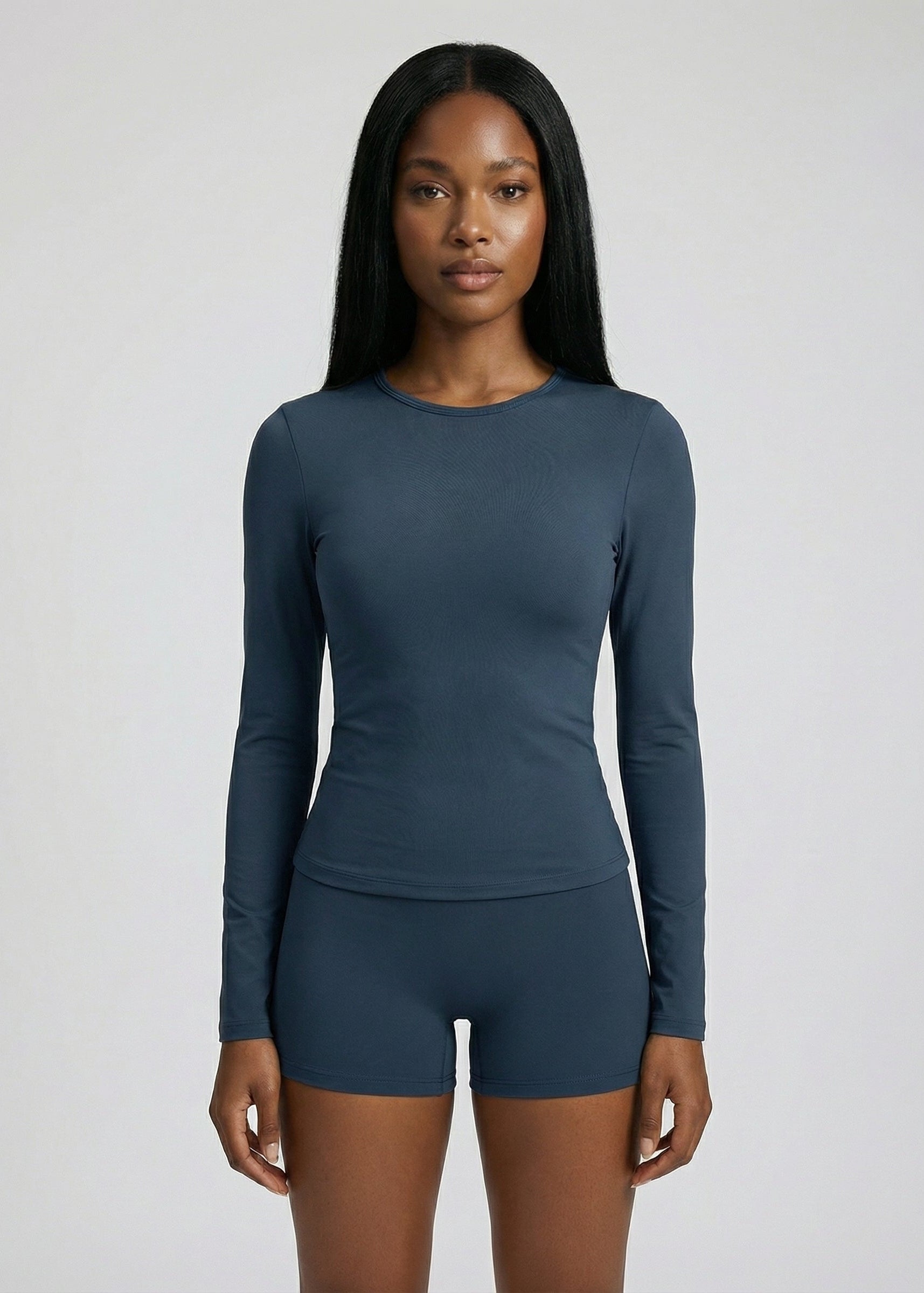 Woman wearing a teal long-sleeve top and shorts on a light gray background